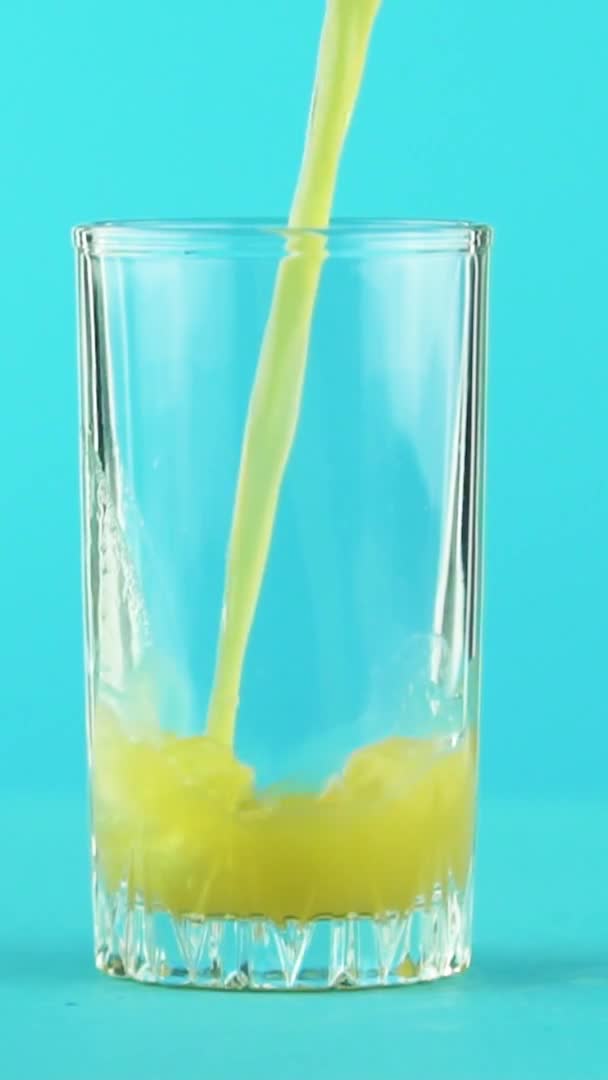 Vídeo vertical Slow motion close-up shot of fruit orange multifruit juice cold beverage pooring into threaded glass blue background in studio — Vídeo de Stock