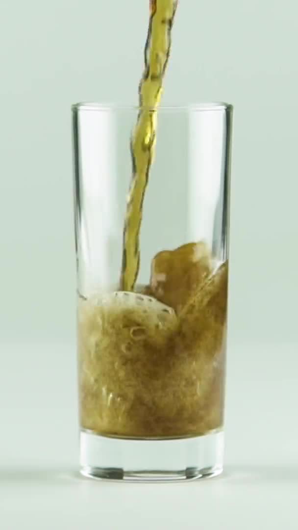 Verticale video Cola wordt gegoten in glas vol bellen en schuim geïsoleerd op witte achtergrond slow motion — Stockvideo