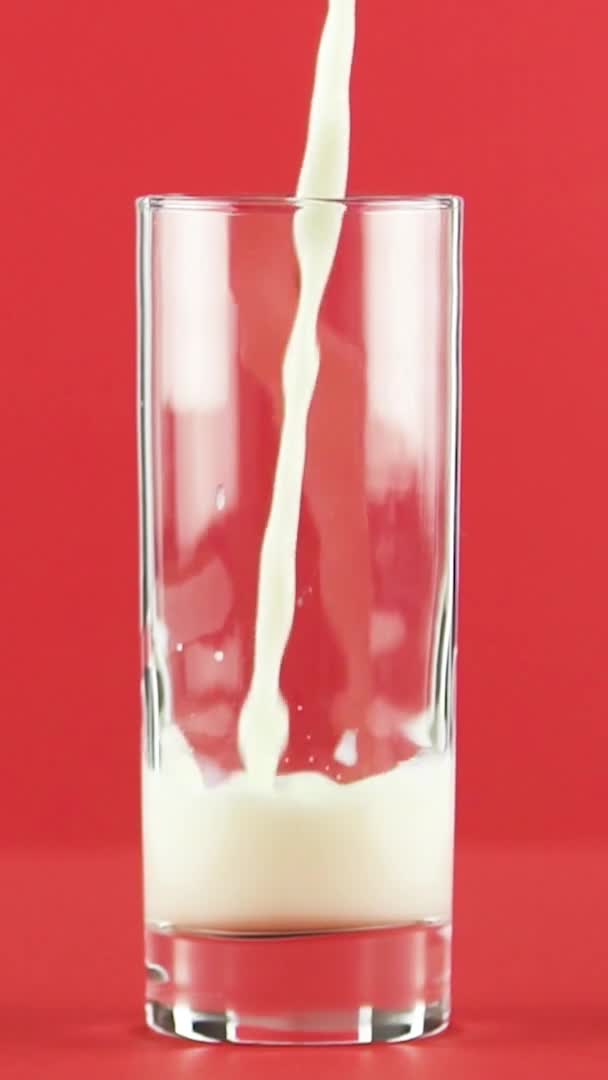 Vídeo vertical Slow motion close-up shot of cold diary milk cold beverage drink pooring into glass red background in studio — Vídeo de Stock