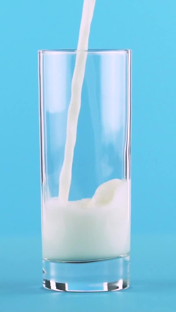 Vídeo vertical Slow motion close-up shot of milk cold beverage pooring into glass blue background in studio — Vídeo de Stock