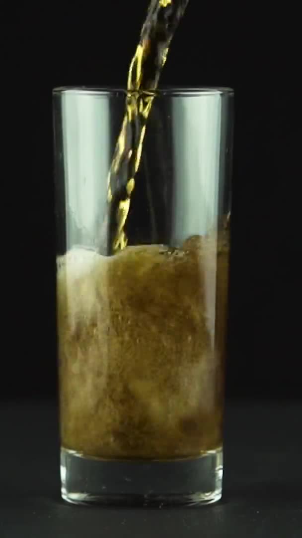 将垂直视频可乐倒入玻璃杯中，玻璃杯中充满泡沫和气泡，并与黑色背景隔离 — 图库视频影像