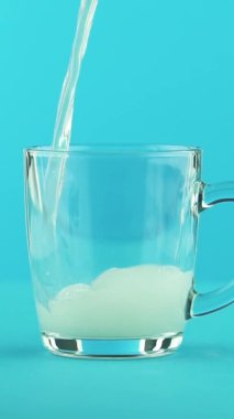 Dikey video. Yavaş çekim. Stüdyoda mavi arka planda cam bardağa sıkışmış meyveli limonata ve soğuk içecek.