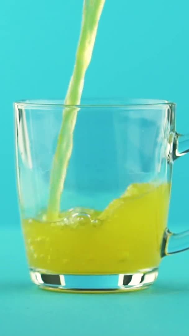 Vídeo vertical Slow motion close-up shot of fruit fizzy orange soda cold beverage pooring into glass mug with rounded handle blue background in studio — Vídeo de Stock