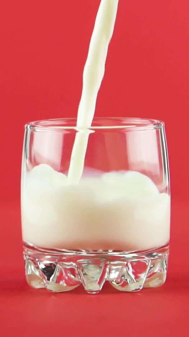 Vídeo vertical Slow motion close-up shot of cold diary milk cold beverage drink pooring into small beautiful glass red background in studio — Vídeo de Stock