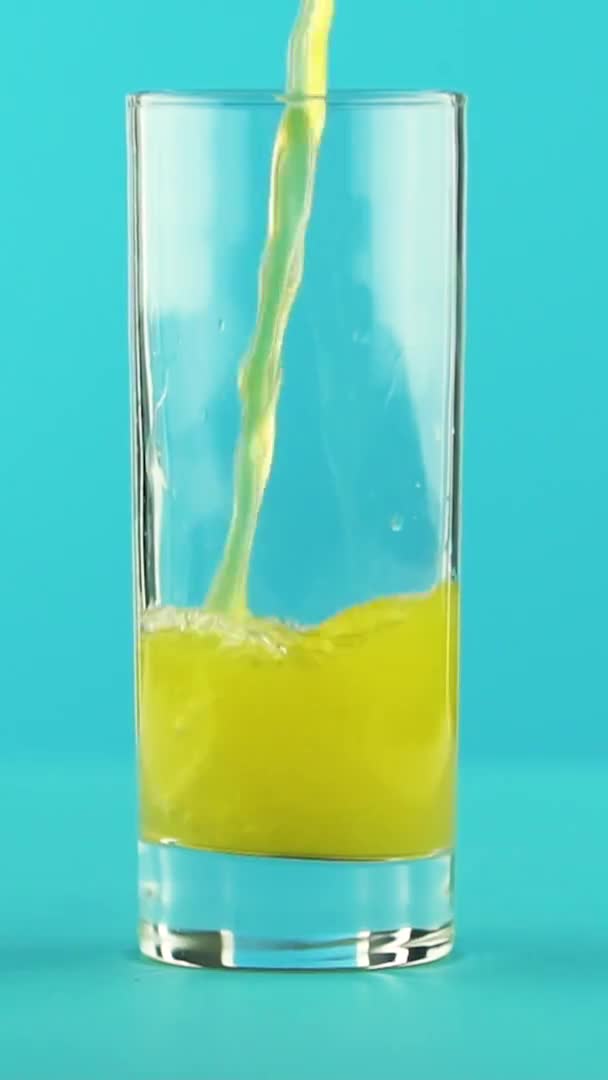 Vídeo vertical Slow motion close-up shot of fruit fizzy orange soda cold beverage pooring into low glass blue background in studio — Vídeo de Stock