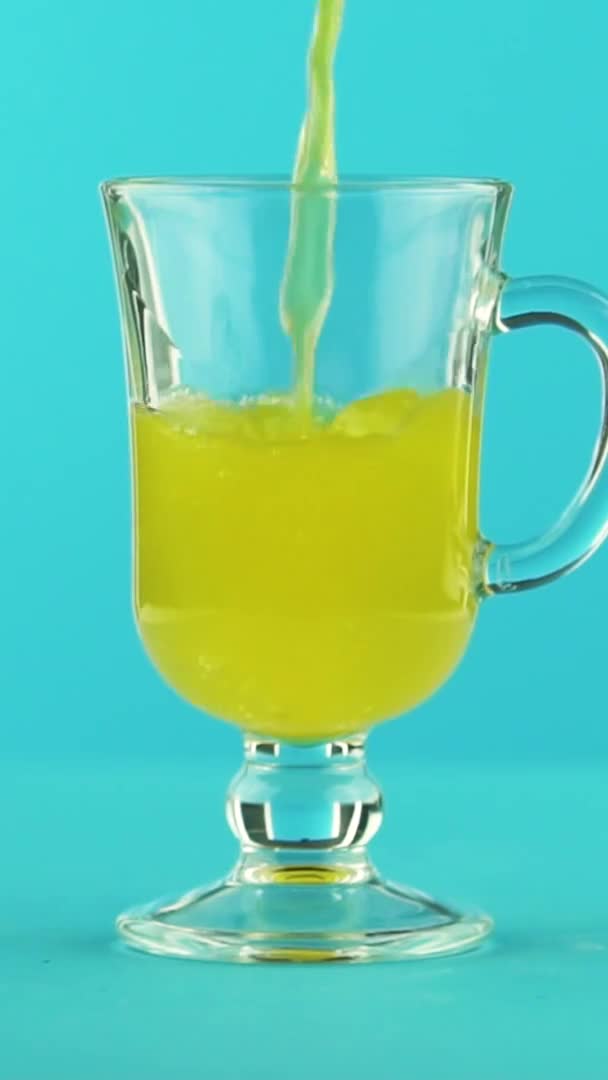 Vídeo vertical Primer plano en cámara lenta de fruta gaseosa naranja gaseosa bebida fría pooring en taza de vidrio latte fondo azul en el estudio — Vídeos de Stock