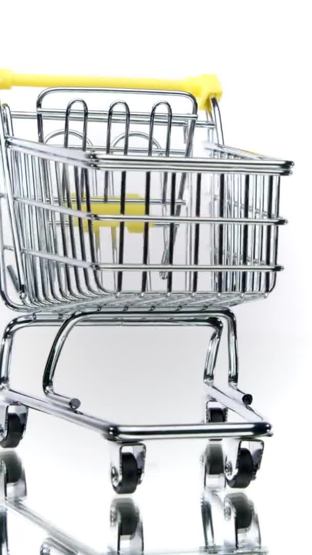 Vídeo vertical Pequeno carrinho de compras vazio girando isolado no fundo branco. Comércio electrónico — Vídeo de Stock