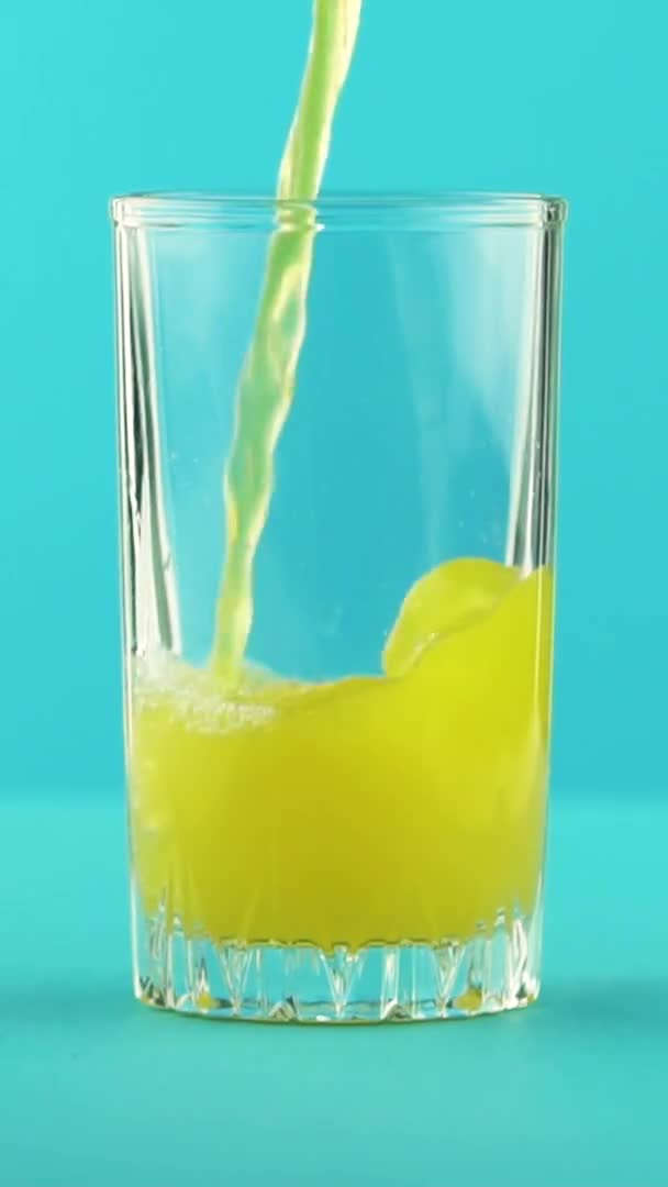 Függőleges videó Lassú mozgás közelkép gyümölcs narancs multifruit lé hideg ital pooring üveg bögre kék háttér stúdió — Stock videók