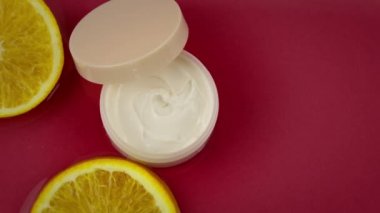 Nemlendirici kremalı kozmetik kavanozu ve su yüzeyinde taze portakal parçaları.