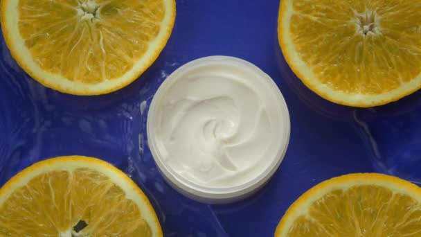 Cosmetische pot met room en verse citrusvruchten in water plons, blauwe achtergrond — Stockvideo