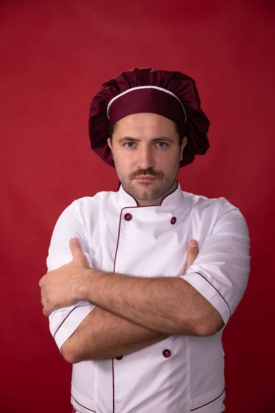 Portret van knappe chef-kok in uniform kijkt naar camera op rode achtergrond — Stockfoto