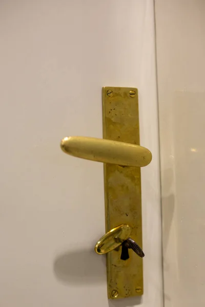 Bronze door handle with key on white smooth door in constructivism style of 20s