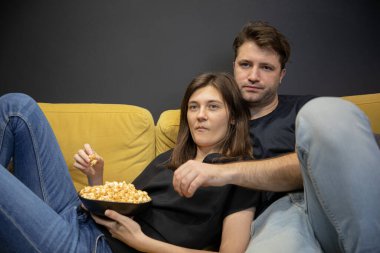 Sakin adam ve kız ellerinde patlamış mısırla kanepede uzanıp televizyon seyrediyorlar.