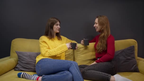 To piger diskuterer sladder sidder på gul sofa og drikker kaffe – Stock-video