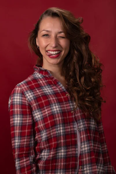 Retrato de mulher bonita se divertindo mostra língua e pisca no fundo vermelho — Fotografia de Stock