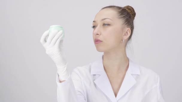Hübsche Dermatologin analysiert wissenschaftlich untermauerte Creme, weißer Laborhintergrund — Stockvideo