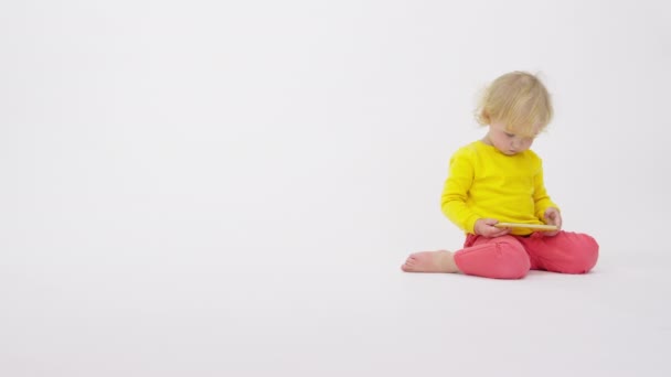 Schattig klein kind met behulp van smartphone kijken educatieve video, witte achtergrond — Stockvideo