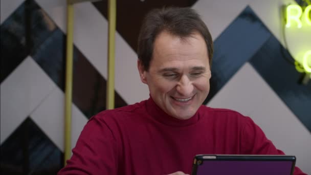 Lächelnder gutaussehender Mann mittleren Alters plaudert im Café mit Tablet — Stockvideo