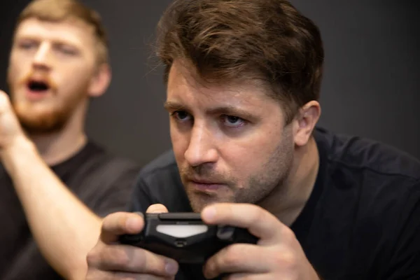 Deux beaux gars jouent passionnément jeu vidéo tenant joystick console dans les mains — Photo