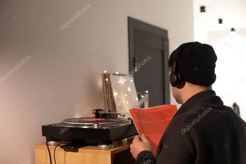 Young unshaven handsome hipster guy puts record on turntable from red envelope