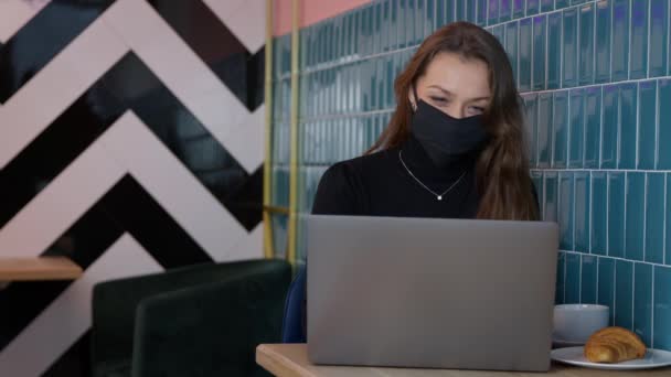 Attraktiv långhårig flicka i svart skyddsmask meddelande i café — Stockvideo