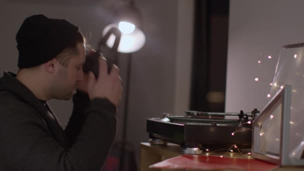 Young unshaven handsome guy takes record off turntable taking his headphones off — Stock Video