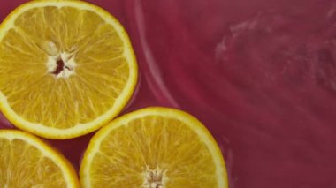 Temiz suda taze portakal parçaları kırmızı arkaplanda sıçramış.