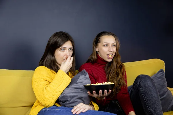 Две симпатичные девушки едят попкорн, пока боятся смотреть телевизор — стоковое фото