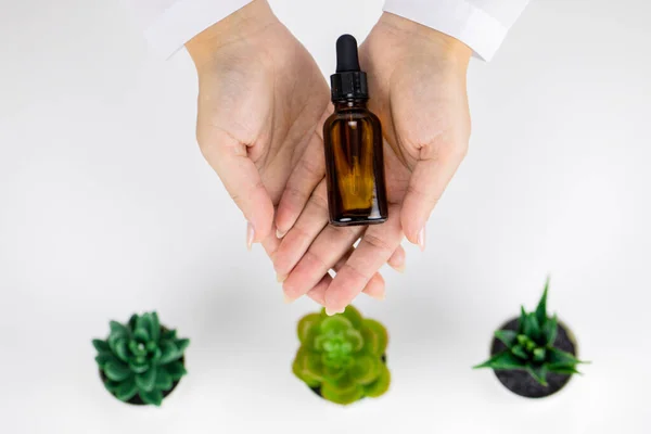 Zbliżenie ręce trzymać szklaną butelkę oleju kosmetycznego na białym tle z roślin — Zdjęcie stockowe