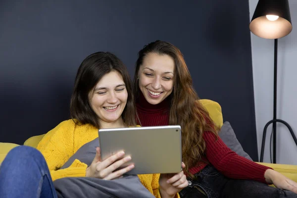 young lesbian couple smiling chatting and messaging sitting on sofa with tablet