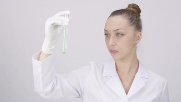 Довольно ученый проверить пробирку с зеленой жидкостью, белый лабораторный фон — стоковое видео