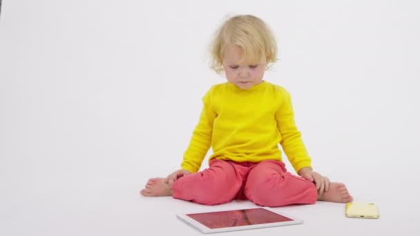 Cute little baby sitting on floor skillfully uses tablet phone, white background — Stock Video