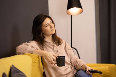 Çekici uzun saçlı esmer kız TV 'de film izlerken uzaktan kumandaya tıklıyor.