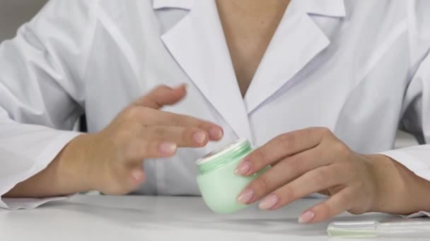 Researcher tests cosmetics from jar in lab dabbing on hand and examining texture — Stock Video