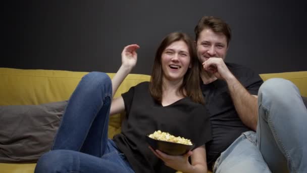 Attraente giovane coppia seduta sul divano con popcorn guardando film in TV — Video Stock