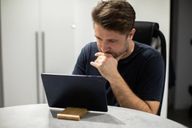 Tıraşsız yakışıklı adam tablet gibi görünüyor, uzaktan çalışıyor.