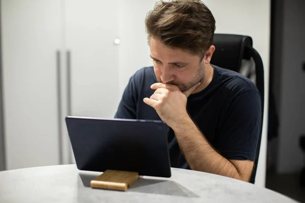 Enfocado chico guapo sin afeitar buscando tableta, trabajando desde casa de forma remota Fotos De Stock Sin Royalties Gratis