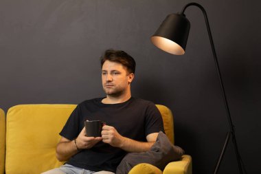 Genç traşsız adam kanepede içki ve uzaktan kumandayla film izliyor.