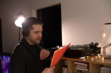 Tıraşsız yakışıklı hippi kırmızı plak zarfına bakar ve müzik dinler.