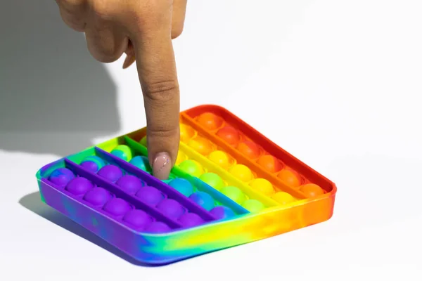 Pop It Fidget juguete, burbujas de empuje de mano femenina en el juego del arco iris, fondo blanco Imagen De Stock