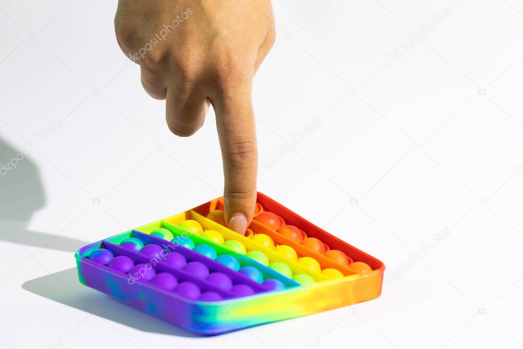 Pop It Fidget toy, female hand push bubbles on rainbow game, white background