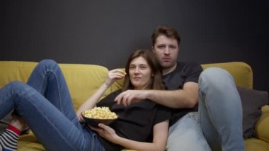 Çekici genç çift kanepede oturup patlamış mısırla TV 'de film izliyor.