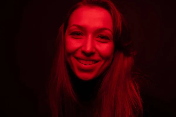 Mujer bonita joven mira a la cámara con sonrisa, contraste luz roja, retrato de arte — Foto de Stock