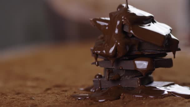 Chocolate derretido derramando sobre pilha de chocolate escuro à mesa com cacau em pó — Vídeo de Stock