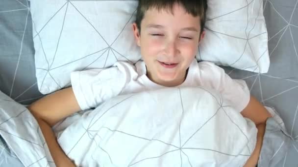 Un băiat zâmbitor care râde zăcând în pat dimineața, fericit concept de copil vesel — Videoclip de stoc