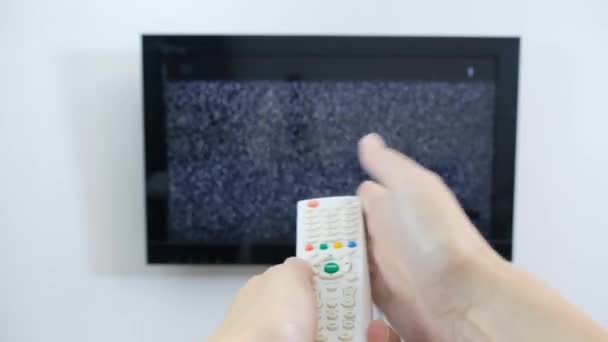 Mano con control remoto de TV frente a la pantalla con ruido blanco - sintonizar los canales de televisión y problemas de conexión — Vídeo de stock