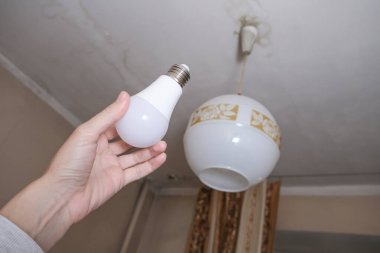 Değiştirmek için öncü ampulü tutan kadın el, onu evde değiştiriyor, ampulü enerji tasarrufu ve ekonomi için lamba tutacağına takıyor, tasarruf ediyor..