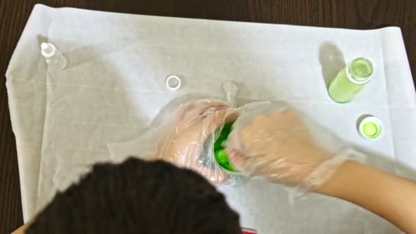 Um menino fazendo lodo verde em casa, projeto DIY, experimento de química, ele derrama os ingredientes em um recipiente e os mistura — Vídeo de Stock