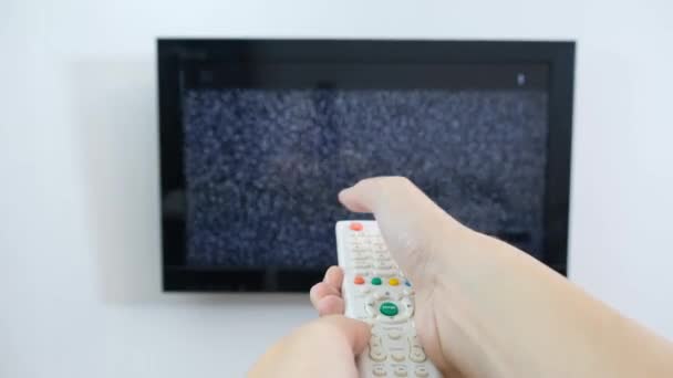 Mano con control remoto de TV frente a la pantalla con ruido blanco - sintonizar los canales de televisión y problemas de conexión — Vídeos de Stock