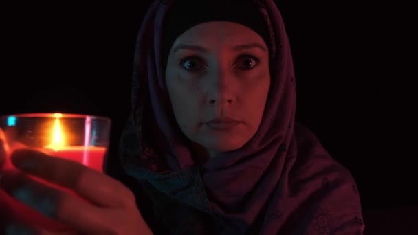 Noční portrét čarodějky, která vrhá kouzlo na červenou svíčku a dělá čarodějnictví, přiblíží svíčku ke kameře a sfoukne plamen. — Stock video
